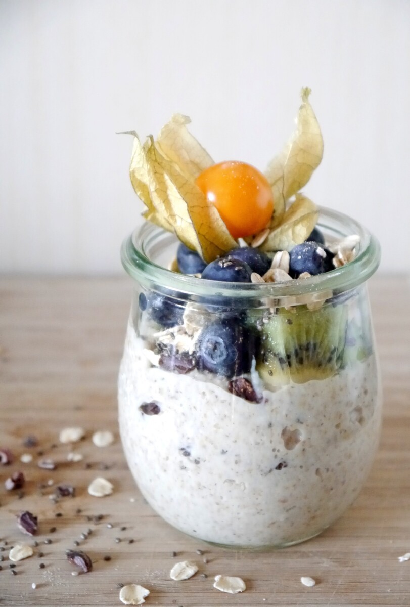 a glass pot of porridge, topped with blueberries and a physalis still with its surrounding case
