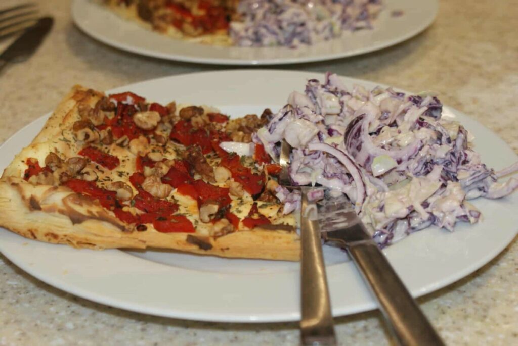 A red pepper and walnut tart, with coleslaw, on a white plate, with cutlery