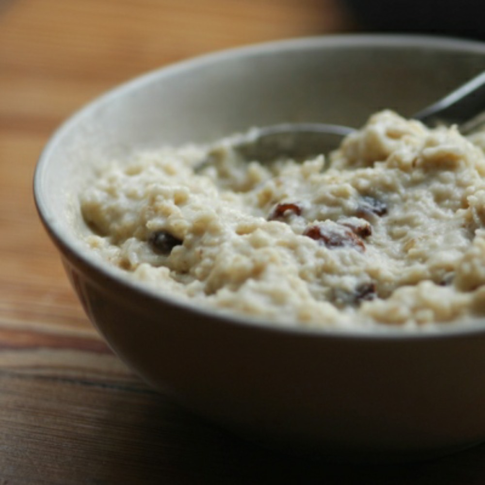 porridge with raisins, in a dark bowl, with a spoon